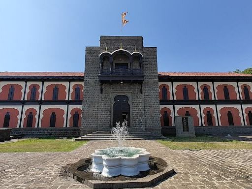 A panoramic view of the Shivsrushti Historical Theme Park, showing a large building with a courtyard and a fountain. The building has a grand and imposing appearance.